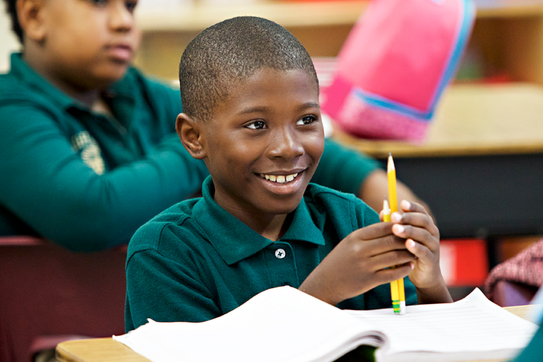 The boy smiles and holds pencils in his hands