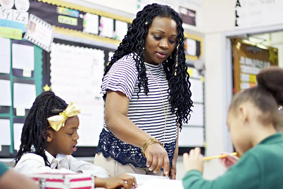 A teacher assisting elementary students with their schoolwork in a classroom.