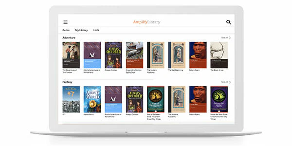 La pantalla de una computadora portátil muestra la Biblioteca Amplify con pestañas para géneros como Aventura y Fantasía, que muestran libros como "El Mago de Oz" y "Frankenstein" en un diseño de cuadrícula.