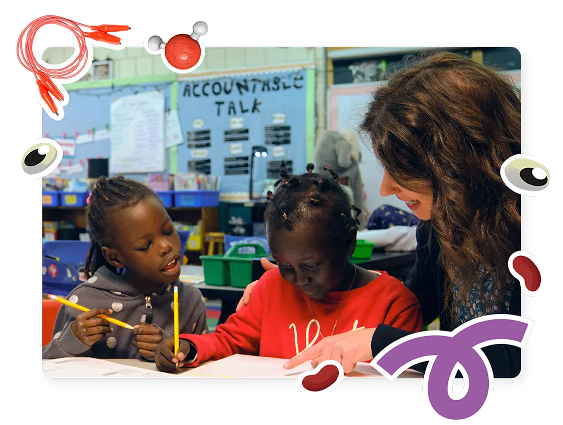 Maestra ayudando a dos niños con una actividad de clase, rodeada de dibujos coloridos y decoraciones.