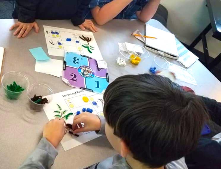 Children playing a board game involving numbers and tokens at a table.