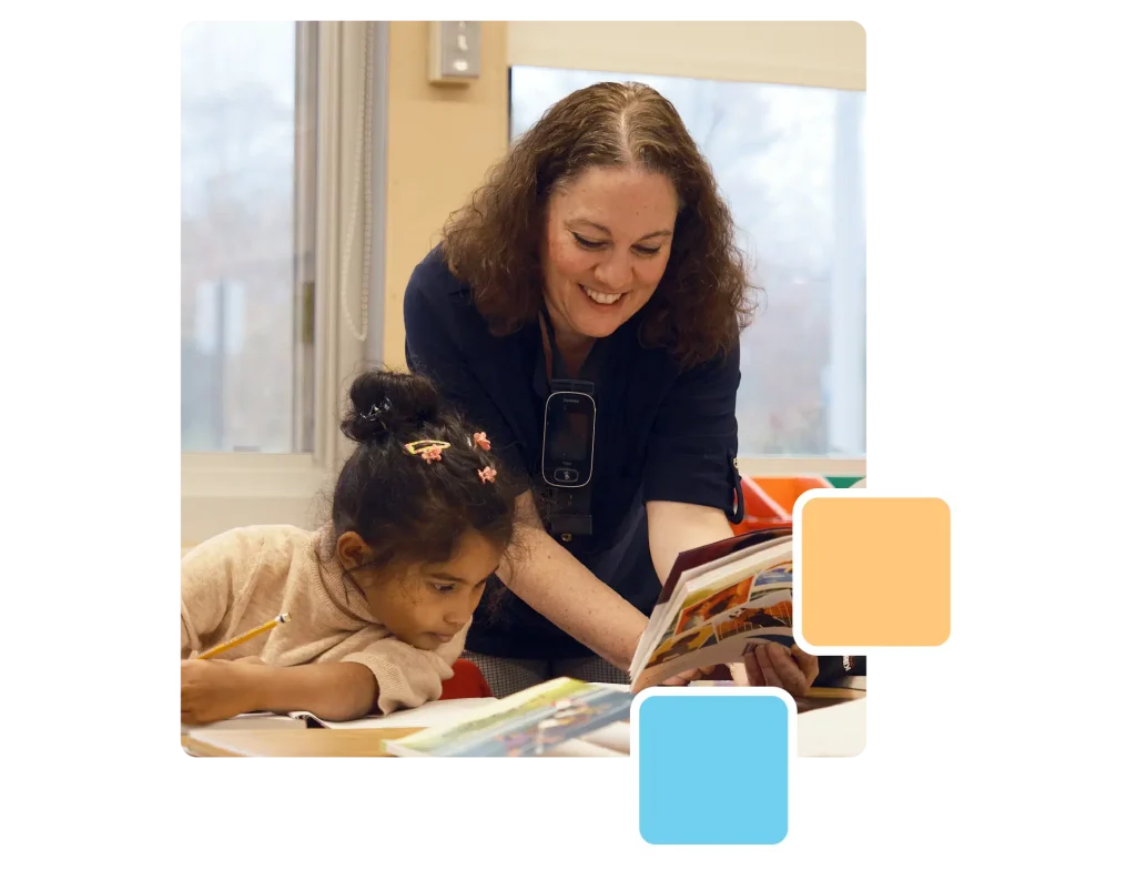 A woman leans over to assist a young girl with her reading and writing at a table in a classroom, with two colored squares overlaid in the foreground.