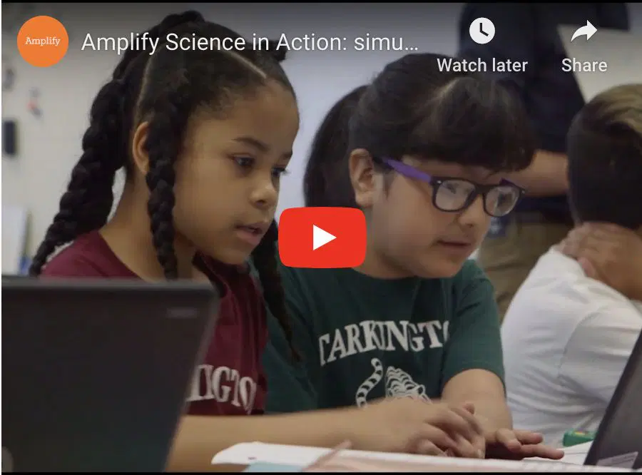 Two girls work together on laptops in a classroom setting, focusing on their screens.