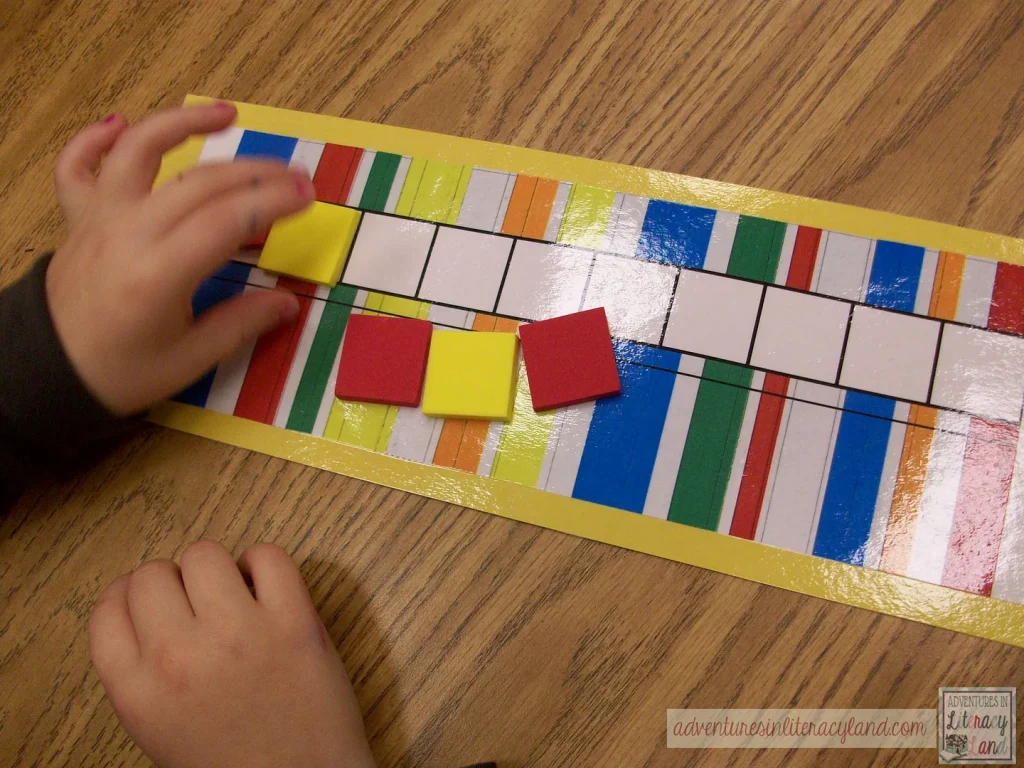 A child arranges red and yellow square tiles on a colorful, laminated grid placed on a wooden table.