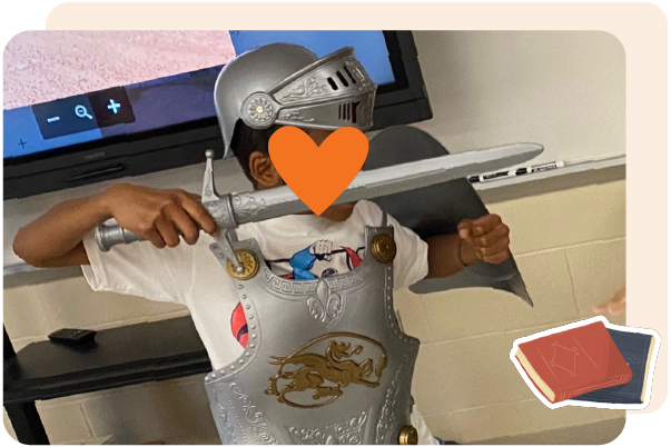 Child wearing a knight costume with helmet, chest plate, and toy sword standing indoors; an orange heart covers the child's face for privacy—a fun way to highlight core knowledge language arts in action.