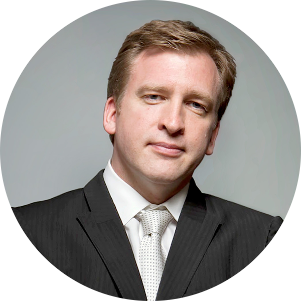 A man in a suit and tie stands against a gray background, arms crossed, exuding confidence as if ready to offer instructional support. He gazes at the camera with an air of determination and expertise.
