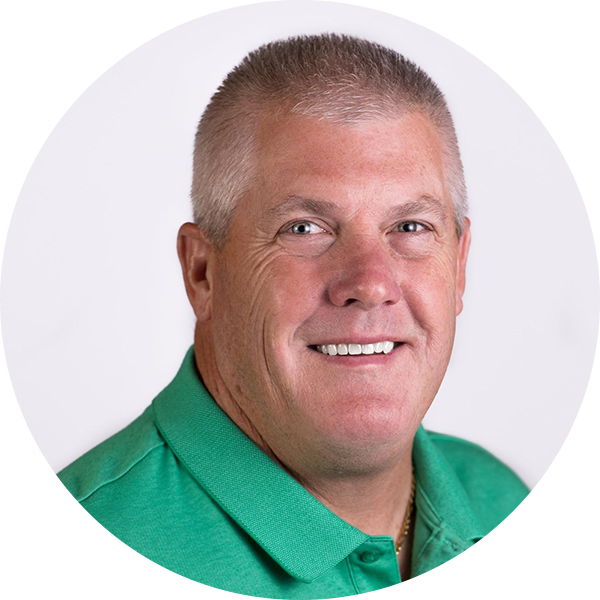 A smiling man with short hair wears a green polo shirt against a plain background, exuding the kind of confidence that comes from teaching an inspiring math lesson.