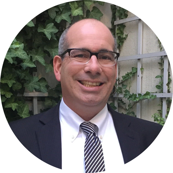 A person in a suit and tie smiles while standing in front of a wall with ivy, embodying the essence of individualized instruction and progress monitoring.