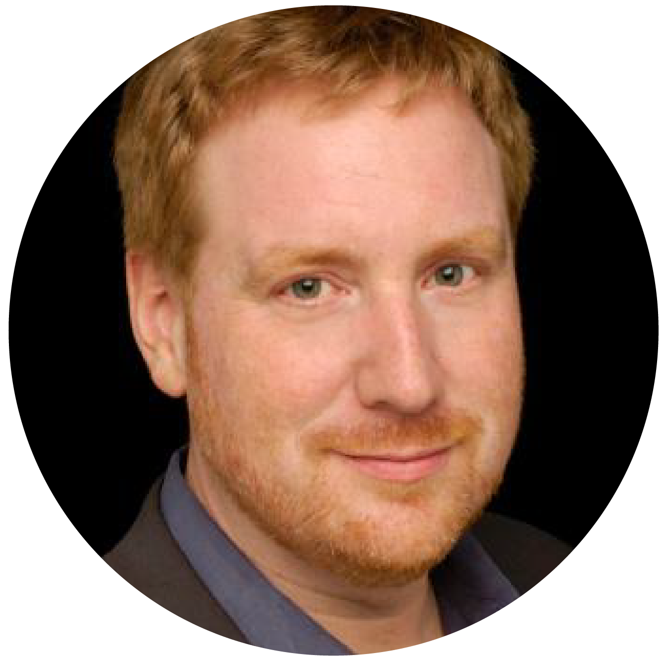 Portrait of a man with short red hair and a beard, wearing a dark jacket over a blue shirt, set against a black background.