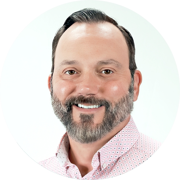 A man with short, dark hair and a full beard smiles confidently. He is wearing a pink patterned shirt and a green jacket, reminiscent of an engaging math lesson. The light gray background subtly complements his dynamic style.