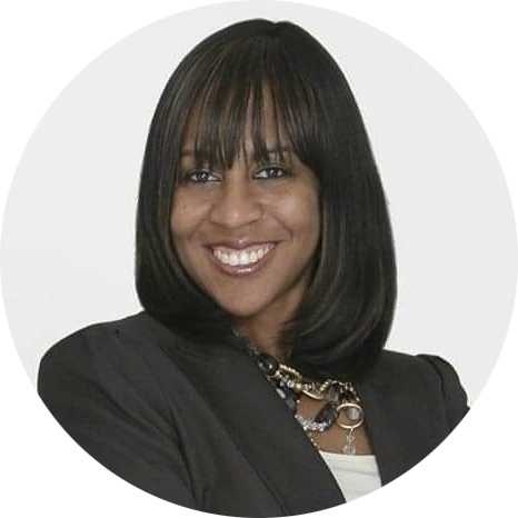 A woman with straight, shoulder-length black hair and bangs, wearing a dark blazer and necklace, is smiling at the camera.